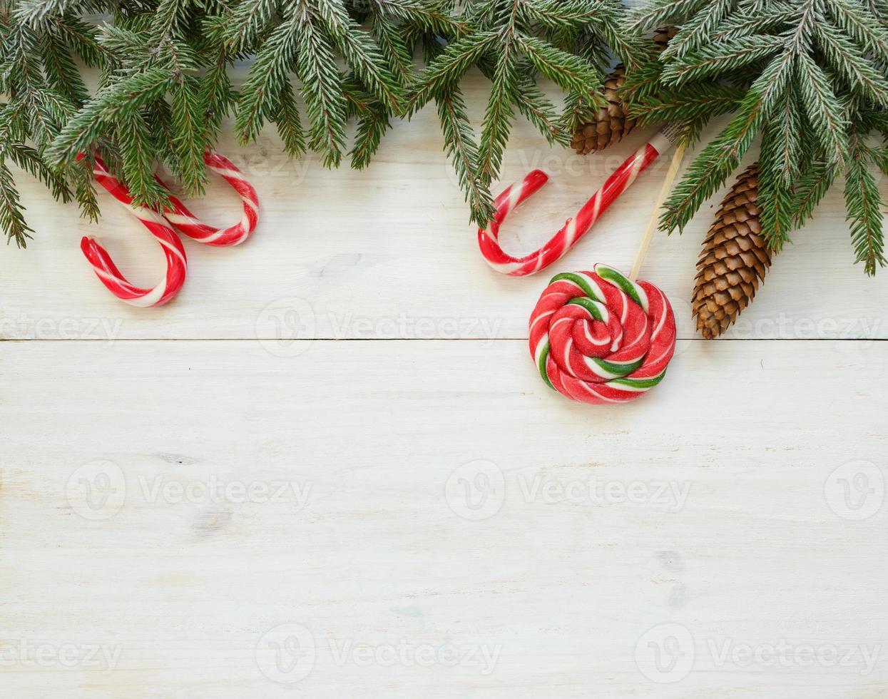 Weihnachten Rand mit Tanne Baum Geäst mit Zapfen und Süßigkeiten Stock auf Weiß hölzern Bretter bereit foto