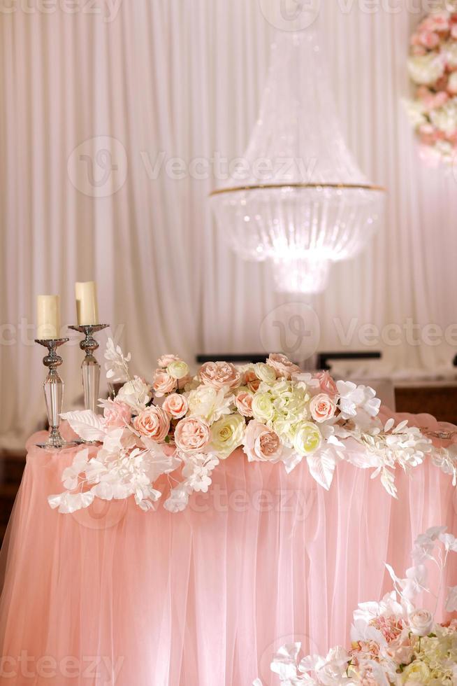 festliche hochzeitstischdekoration mit kristall-kronleuchtern, goldenen leuchtern, kerzen und weiß-rosa blumen. stilvoller Hochzeitstag. foto