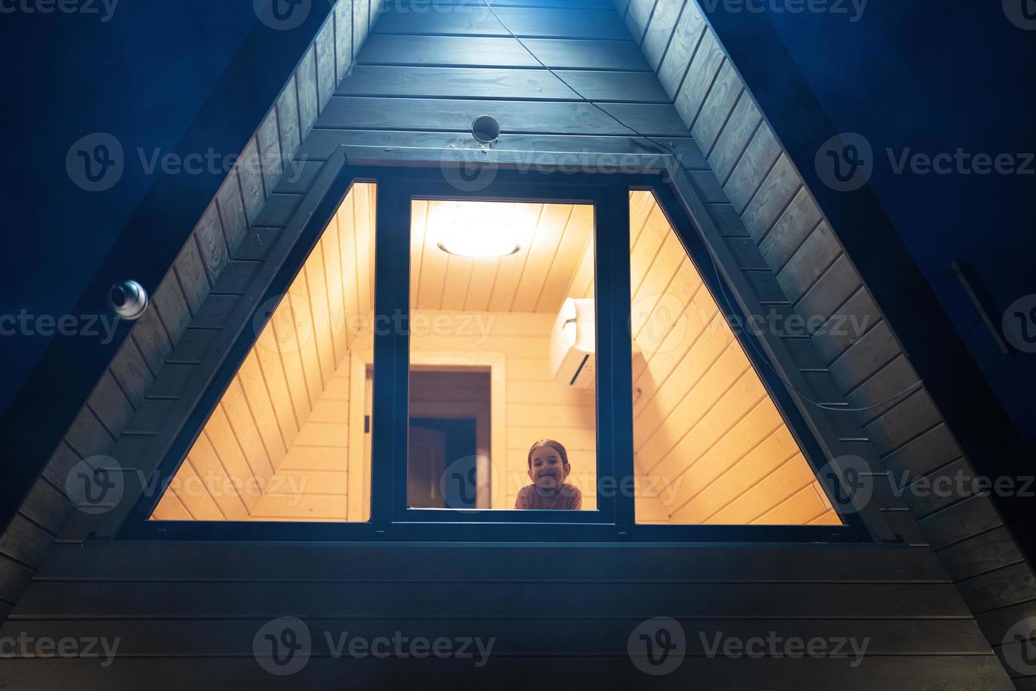 vansicht durch das Fenster von Baby Mädchen im Dreieck Land Haus beim Nacht. foto