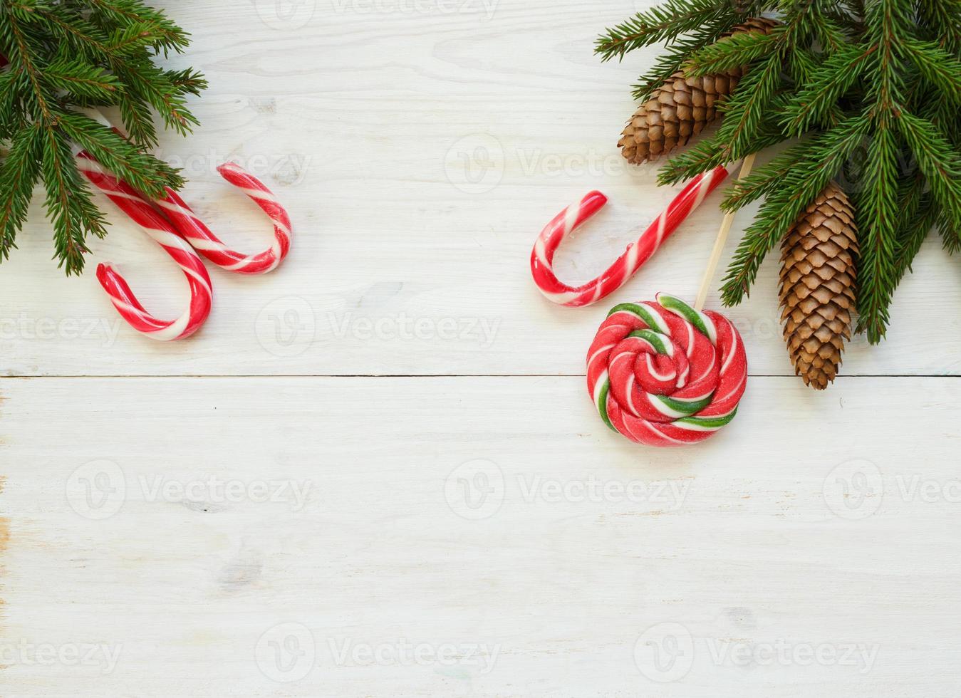 Weihnachten Rand mit Tanne Baum Geäst mit Zapfen und Süßigkeiten Stock auf Weiß hölzern Bretter bereit foto