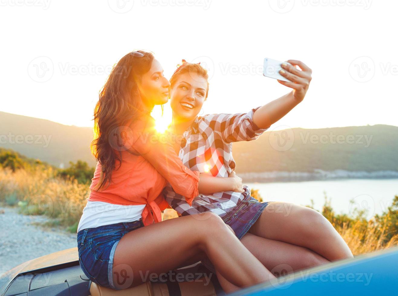 zwei jung schön Mädchen sind tun Selfie im ein Cabrio foto