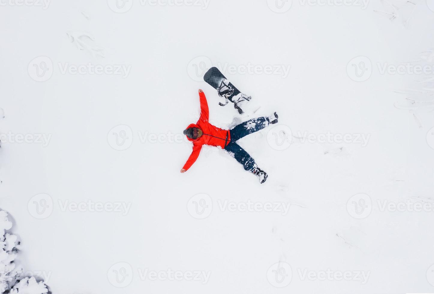 Antenne Aussicht von ein Mann Lügen im das Schnee Nächster zu seine Snowboard foto
