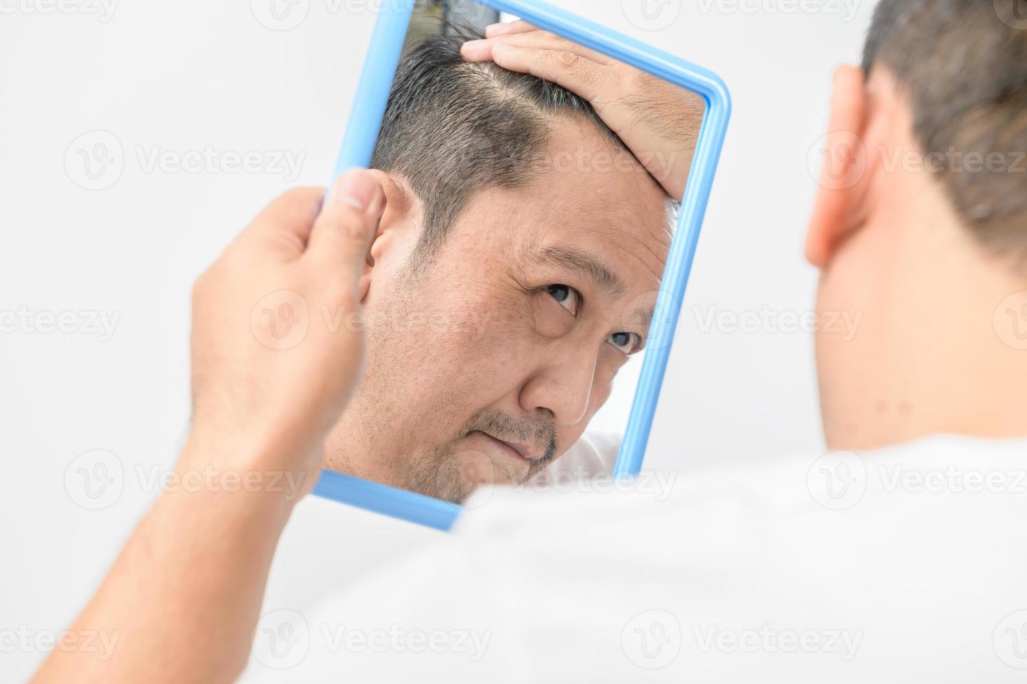 asiatisch mittleren Alters Mann war suchen im das Spiegel und Sorge Über Haar Verlust oder Haar grau foto