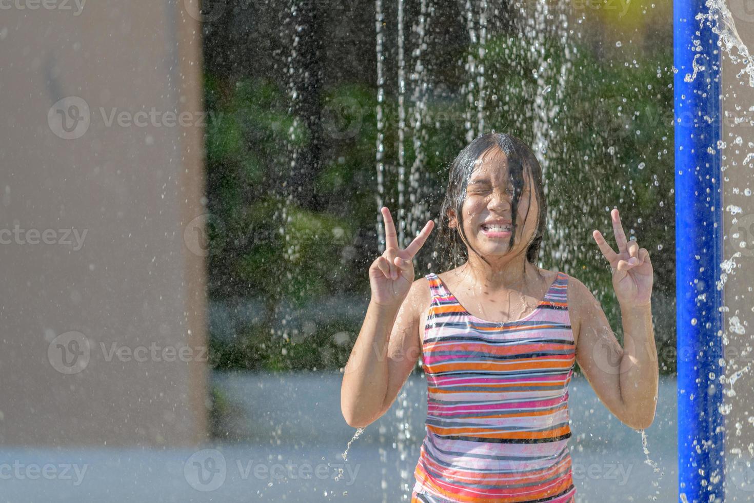 glücklich Mädchen tragen ein Badeanzug abspielen Wasser von das Dusche im das Sommer. foto