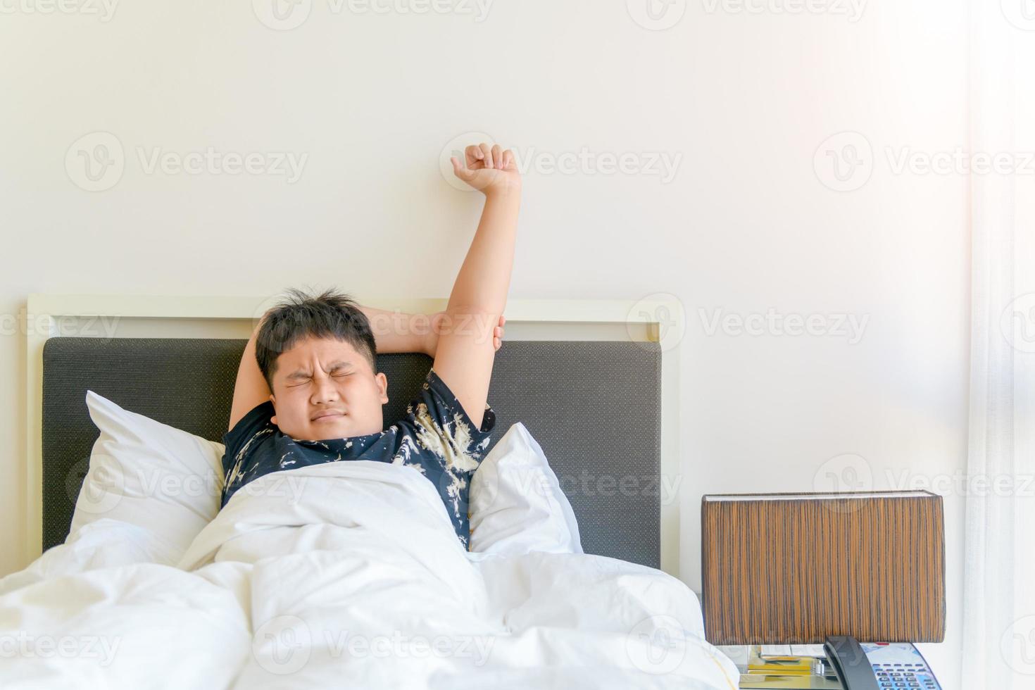 fettleibig Junge aufwachen oben und strecken Arm auf Bett im Morgen. foto