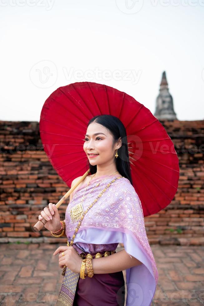 schön thailändisch Mädchen im traditionell Kleid Kostüm rot Regenschirm wie thailändisch Tempel wo ist das Öffentlichkeit Ort, thailändisch Frau im traditionell Kostüm von Thailand. foto