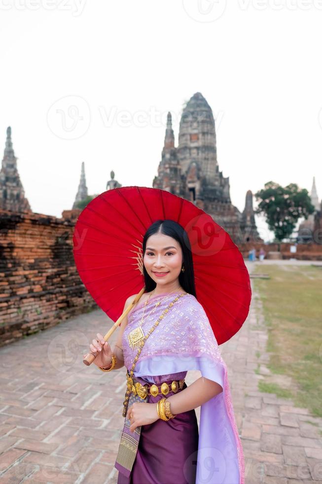 schön thailändisch Mädchen im traditionell Kleid Kostüm rot Regenschirm wie thailändisch Tempel wo ist das Öffentlichkeit Ort, thailändisch Frau im traditionell Kostüm von Thailand. foto