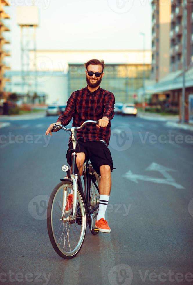 jung Mann im Sonnenbrille Reiten ein Fahrrad auf Stadt Straße foto