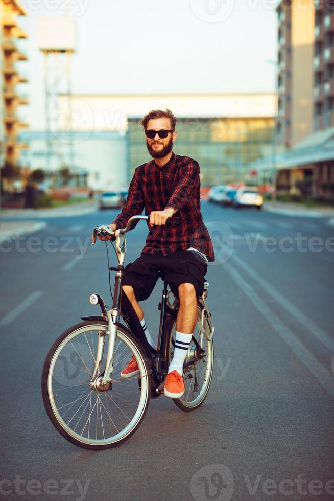 stilvoll Mann im Sonnenbrille Reiten ein Fahrrad auf Stadt Straße foto