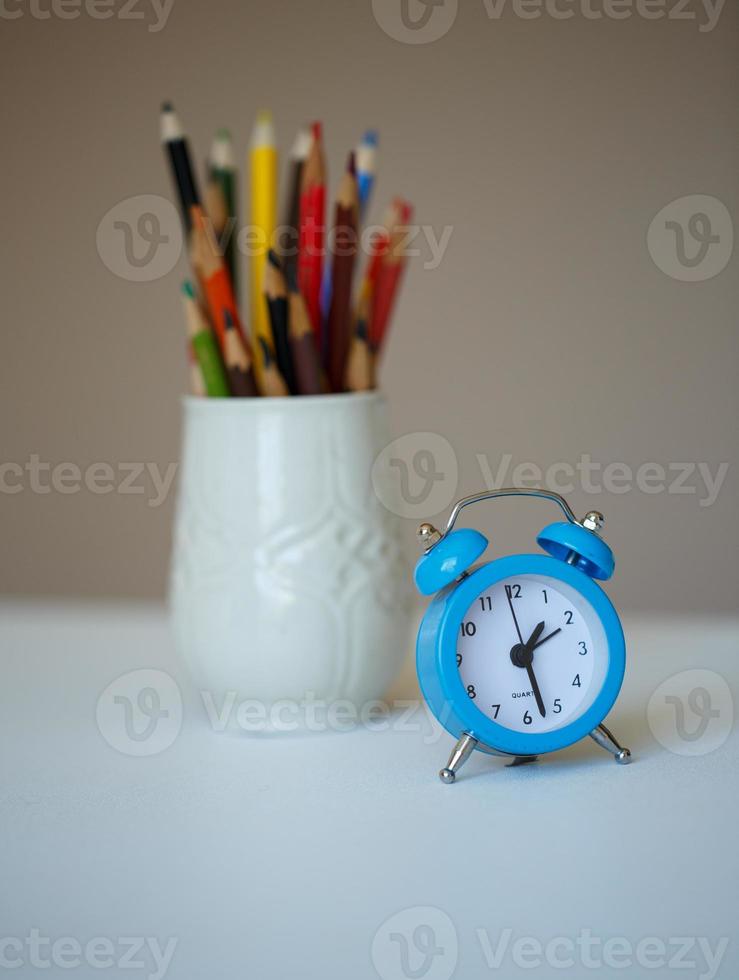 wenig Blau Alarm Uhr und ein Glas mit farbig Bleistifte auf ein Tabelle foto