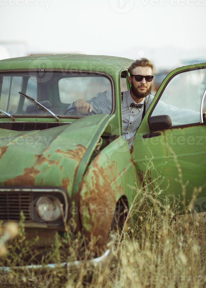 jung stilvoll gut aussehend Mann, tragen Hemd und Sonnenbrille, Fahren alt Auto foto