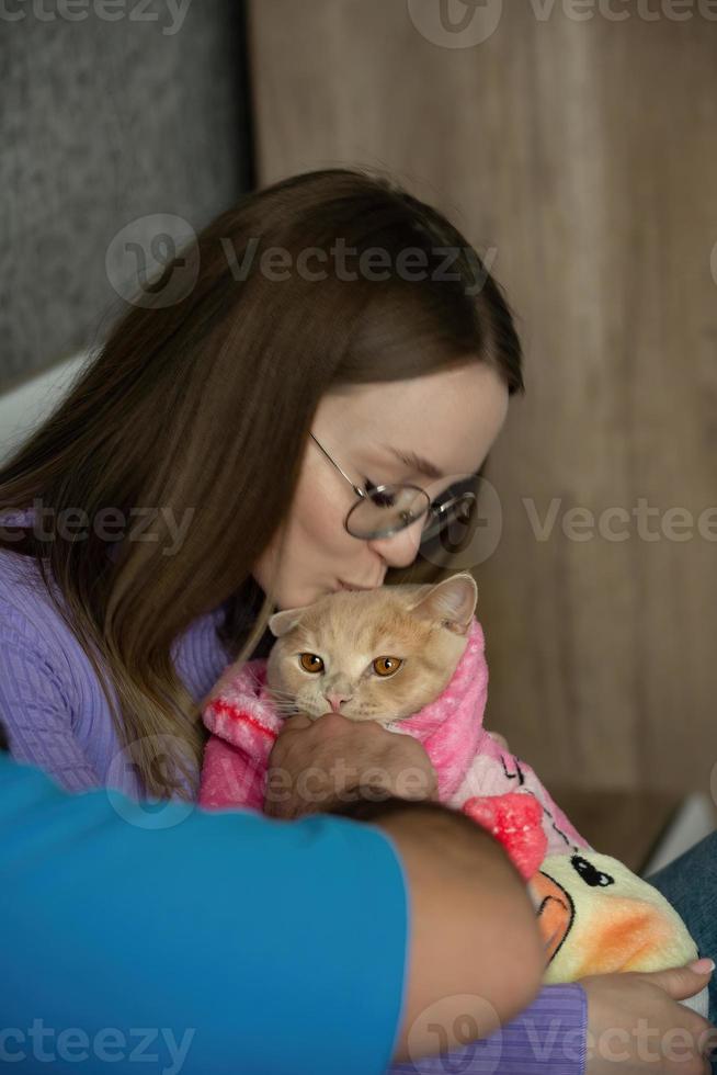 ein jung Frau im ihr Schlafzimmer hält ihr Haustier Katze eingewickelt im ein Baby Decke im ihr Waffen. Liebe und Pflege zum Tiere, kinderlos Frau. Behandlung Tiere mögen Ihre Kinder foto