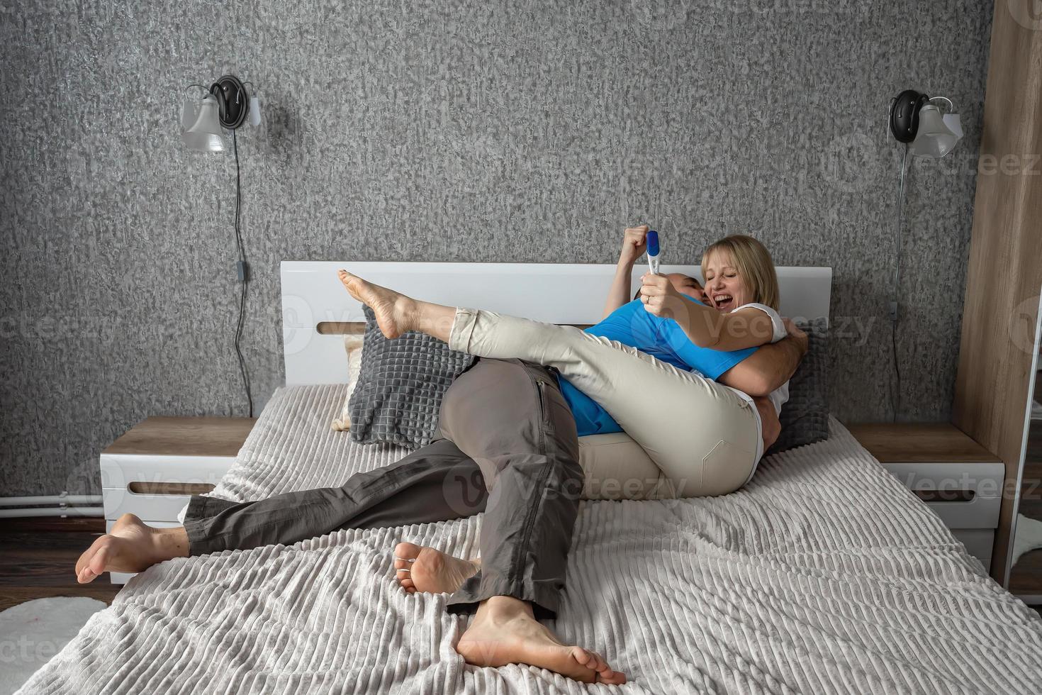 glücklich Mann und Ehefrau jubeln beim ein positiv Schwangerschaft Prüfung auf das Bett im ihr Schlafzimmer. gut Nachricht, Familie Planung, Vaterschaft und Erwartung foto