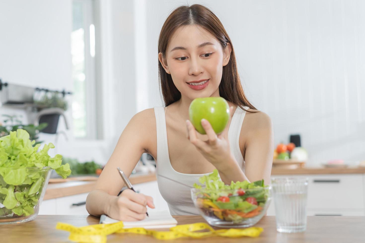 Diät, Diät asiatisch jung Frau Arbeiten, schreiben Diät planen richtig Ernährung, halt Grün Apfel, Gemüse Salat ist Essen zum gut Gesundheit nicht wählen Essen Müll Lebensmittel. Ernährungsberater weiblich, Gewicht Verlust Person. foto