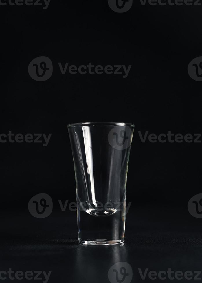 Vertikale Schuss von leeren Glas von Wodka auf schwarz Hintergrund. ein leeren trinken transparent Glas auf ein schwarz Hintergrund. isolieren. Kopieren Raum foto