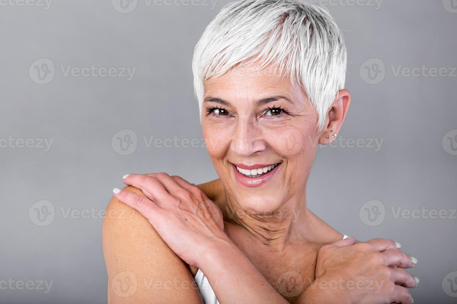 Porträt von ein lächelnd Senior Frau suchen beim Kamera. Nahansicht Gesicht von reifen Frau nach Spa Behandlung isoliert Über grau Hintergrund. Antialterung Konzept. foto