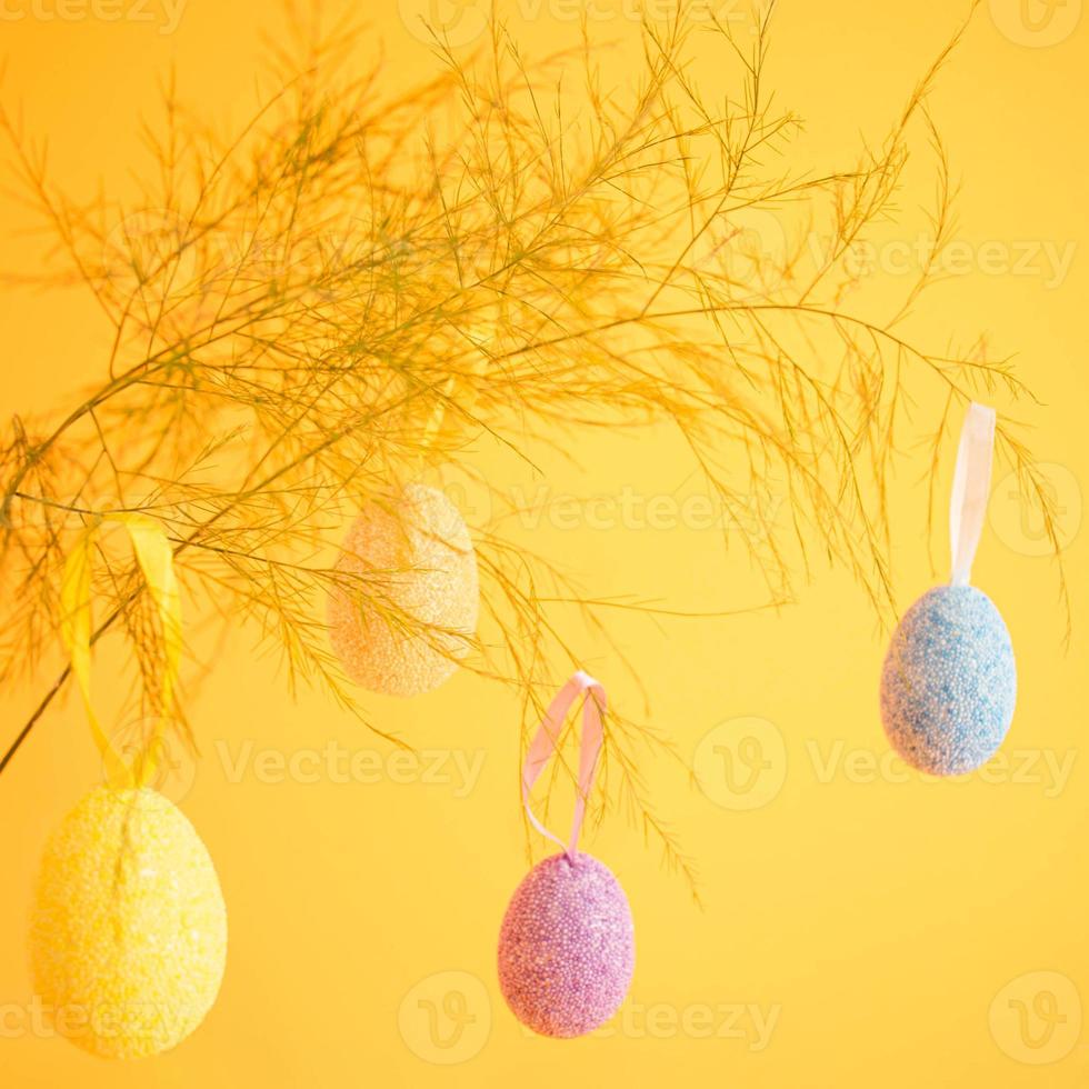 Mehrfarbig Ostern Eier hängend von das Zweig, platziert auf ein hell Gelb Hintergrund foto
