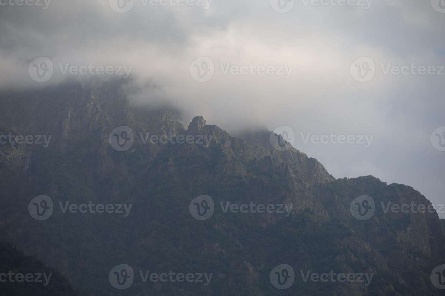 dunkel atmosphärisch surreal Landschaft mit ein dunkel felsig Berg Gipfel im niedrig Wolken im ein grau wolkig Himmel. ein grau niedrig Wolke auf ein hoch Gipfel. foto