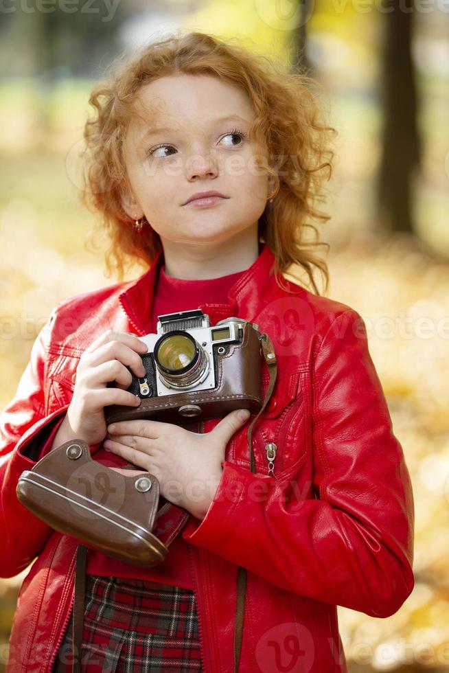 wenig rothaarig Mädchen mit ein retro Kamera auf ein Herbst hintergrund.wenig rothaarig Mädchen mit ein retro Kamera auf ein Herbst Hintergrund. foto