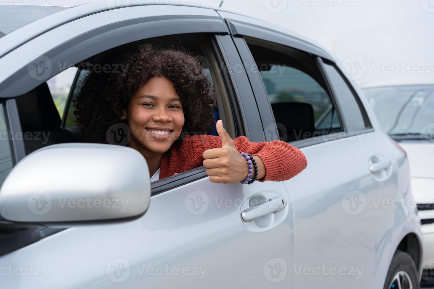 junge frau, halb asiatin, halb afrikanerin, zeigt daumen nach oben im neuen modernen auto. Aufregung der jungen Frau erster Roadtrip nach bestandener Führerscheinprüfung. Fühlt sich gut an, nachdem man ein neues Auto bekommen hat. foto