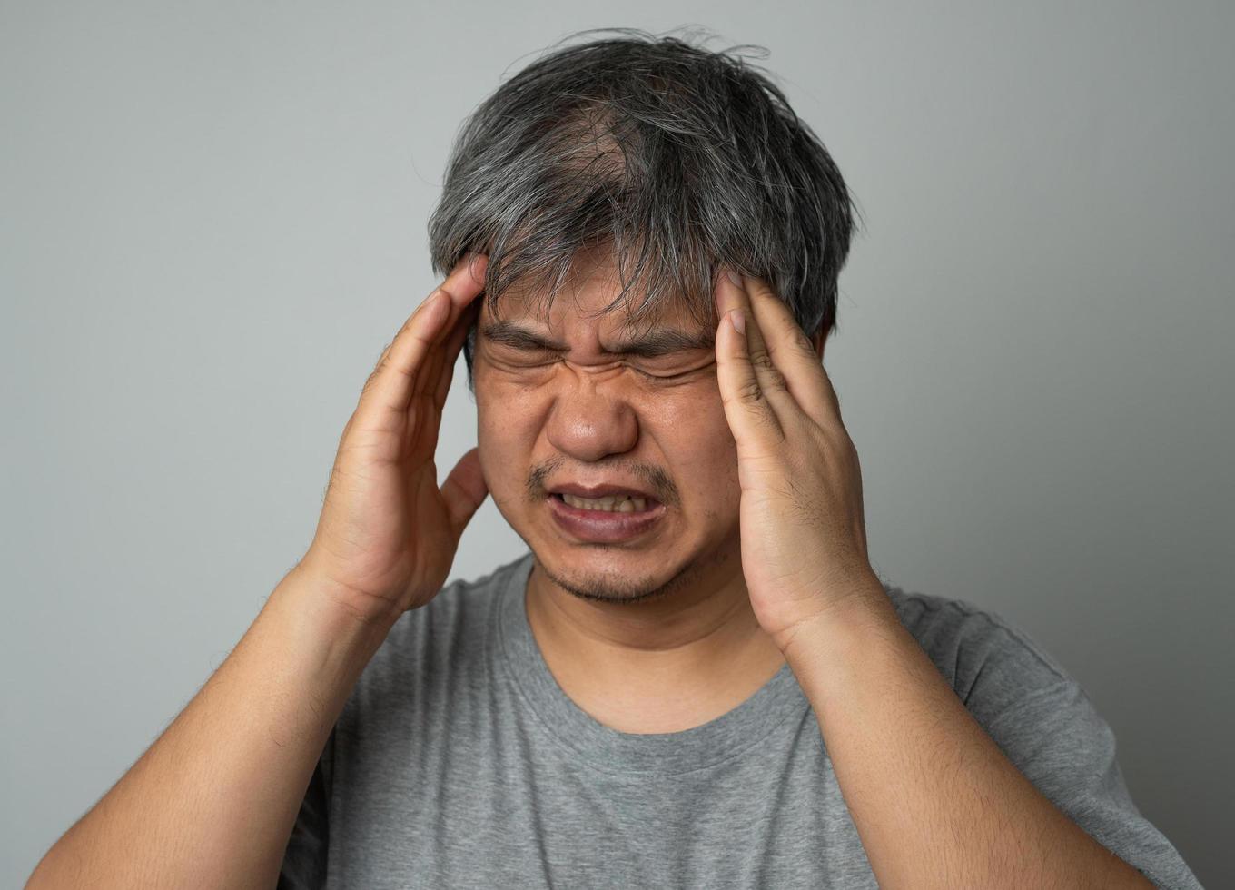 kranker asiatischer mann, der eine medizinische gesichtsmaske trägt und eine hand nimmt, um die kopfschmerzen zu halten. konzept des schutzes pandemie coronavirus und atemwegserkrankungen foto