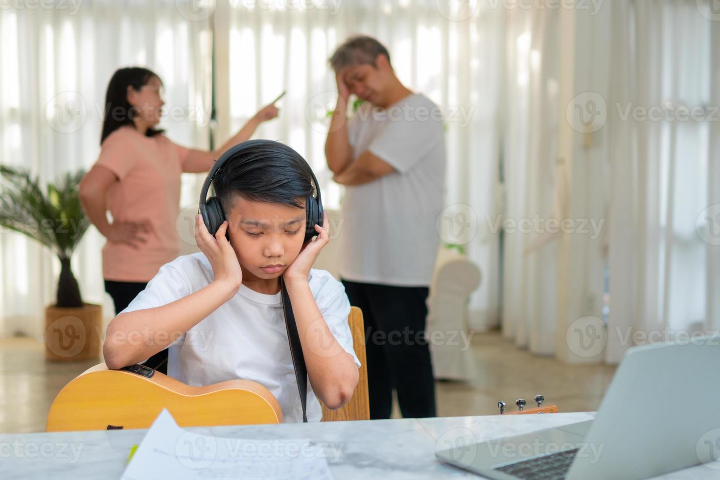 asiatischer junge, der kopfhörer trägt und laute musik spielt. um keinen Streit zu hören, während Eltern zu Hause kämpfen oder streiten. unglückliches Problem in der Familie, häusliche Probleme in der Familie. foto