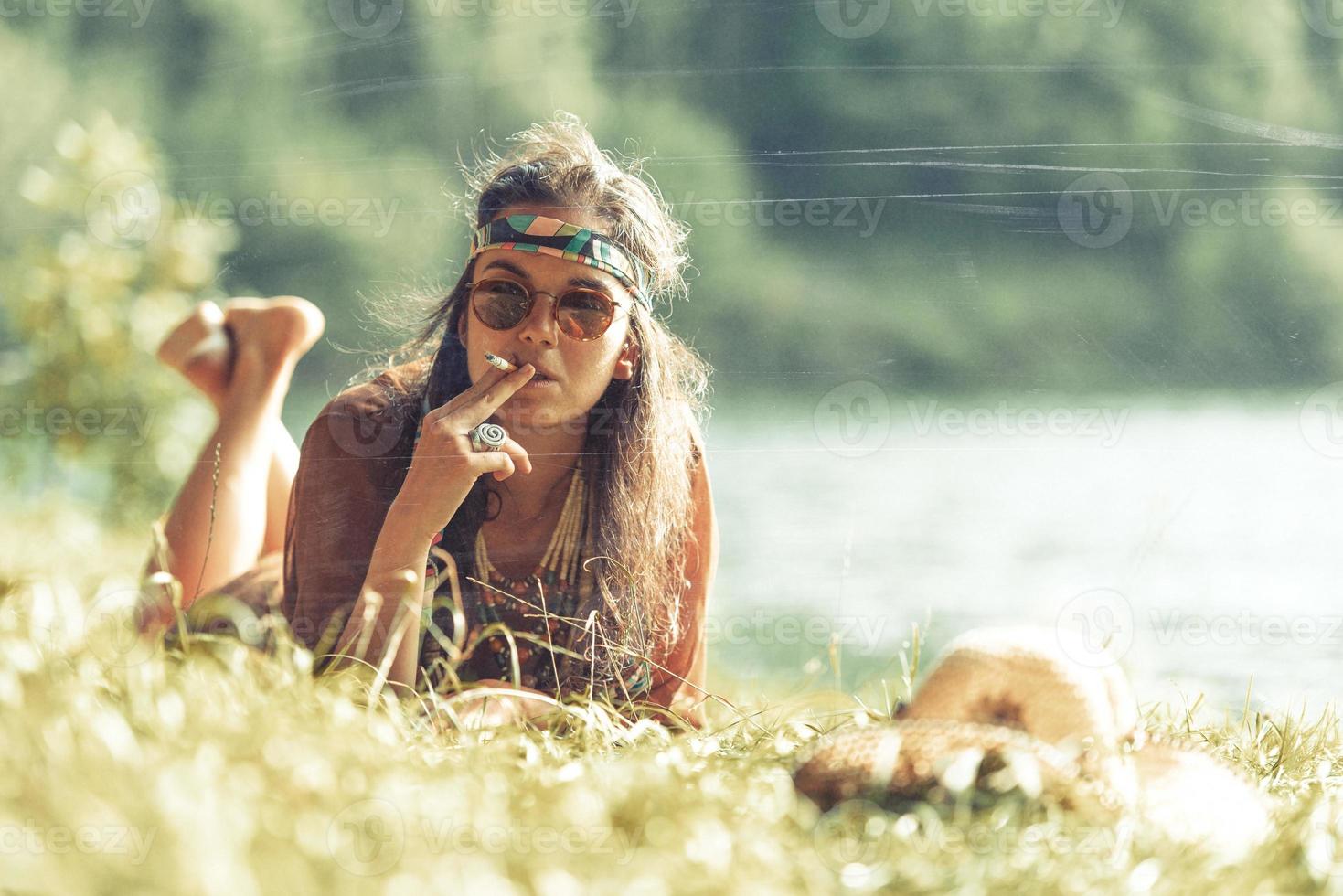 hübsches freies Hippie-Mädchen, das auf dem Gras raucht, Fotoeffekt des Weinleseeffekts foto