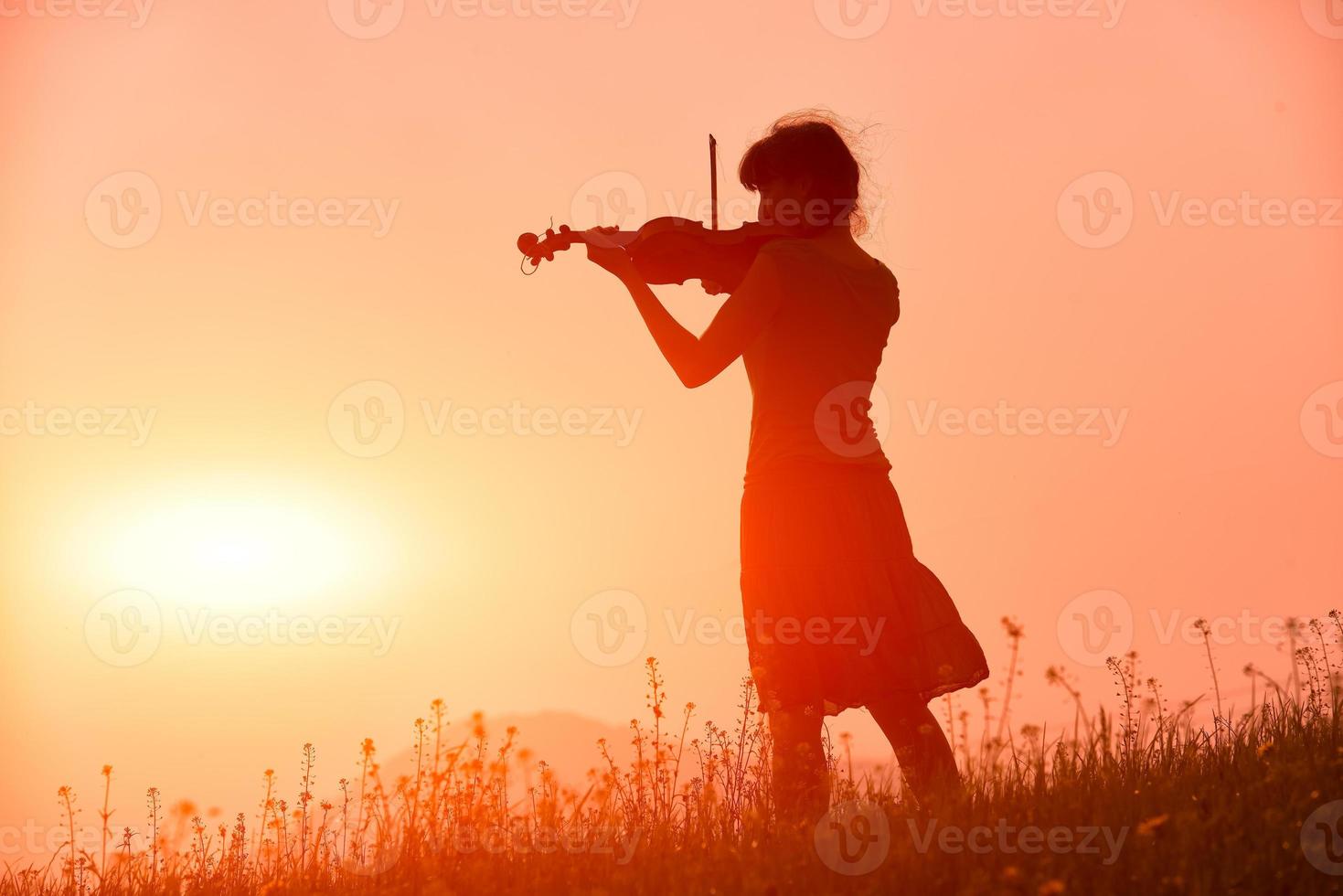 Frau, die eine Geige in einem roten Sonnenuntergang in der Natur spielt foto