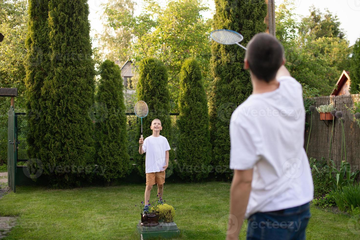 heiter Papa draußen spielen Badminton mit seine Sohn im ein Weiß T-Shirt foto