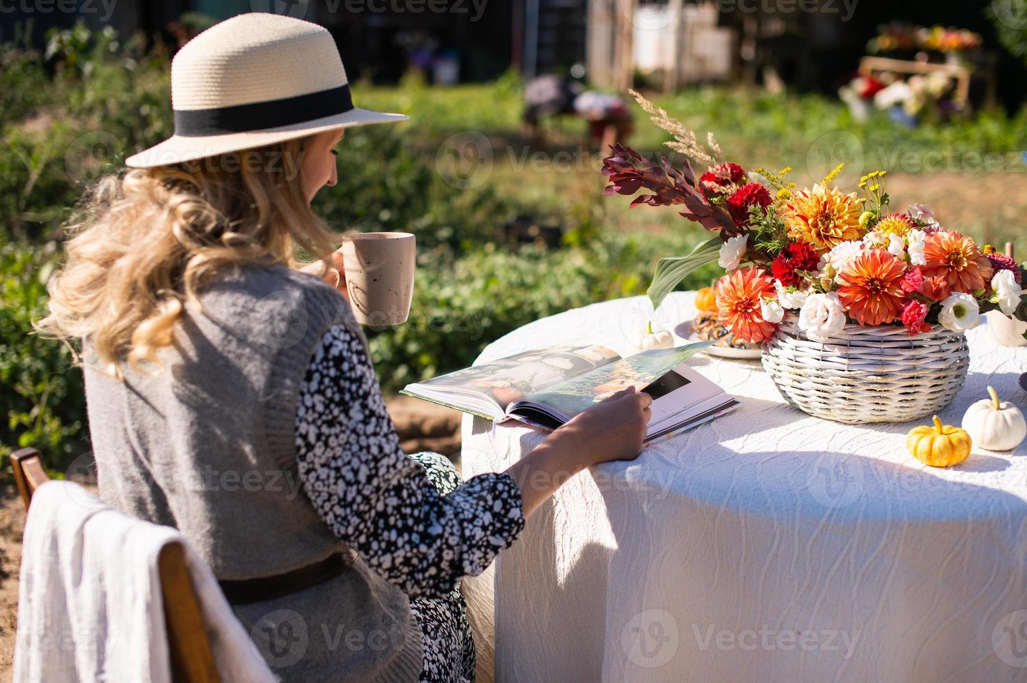 ein Frau flippt durch ein Buch und Getränke ein heiß trinken beim ein Tabelle mit Blumen auf das Straße foto