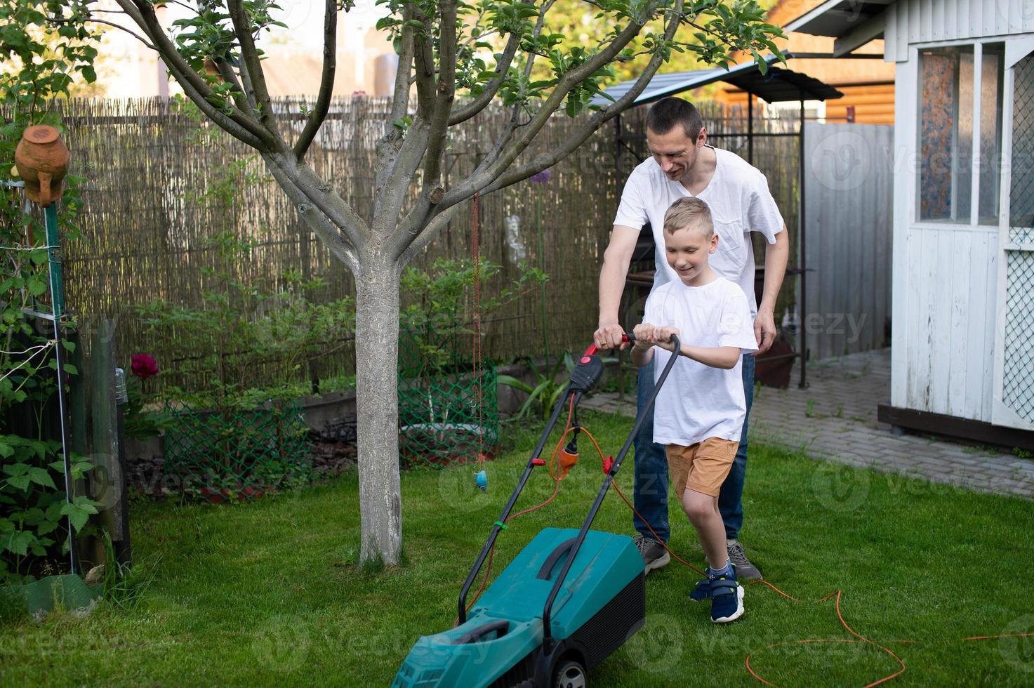 Papa und seine neugierig Sohn mähen das Grün Rasen in der Nähe von das Haus. foto