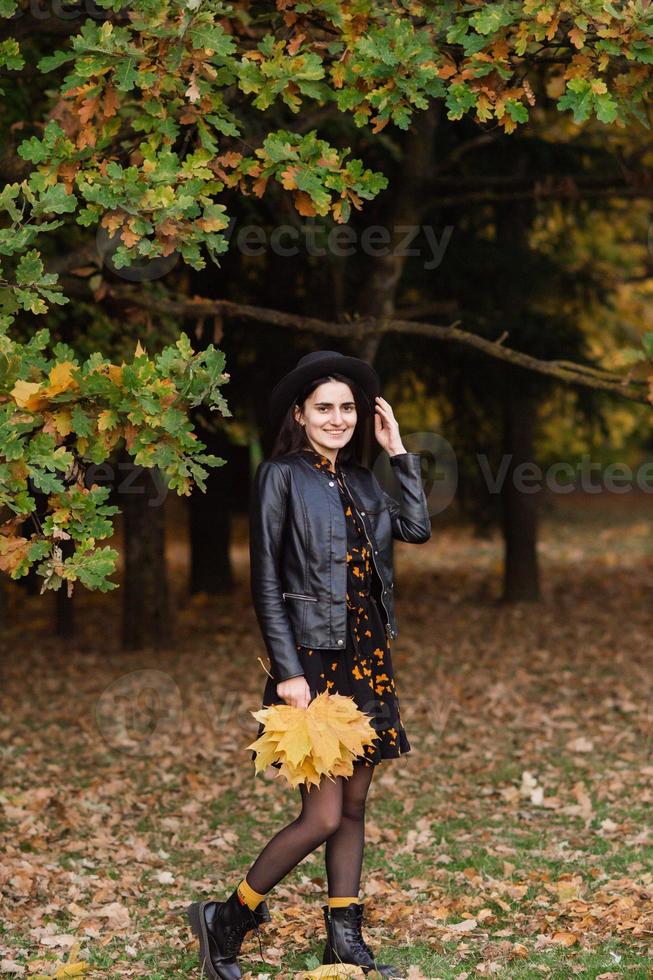 ein Mädchen im ein schwarz Hut hält Gelb Herbst Blätter im ihr Hände foto