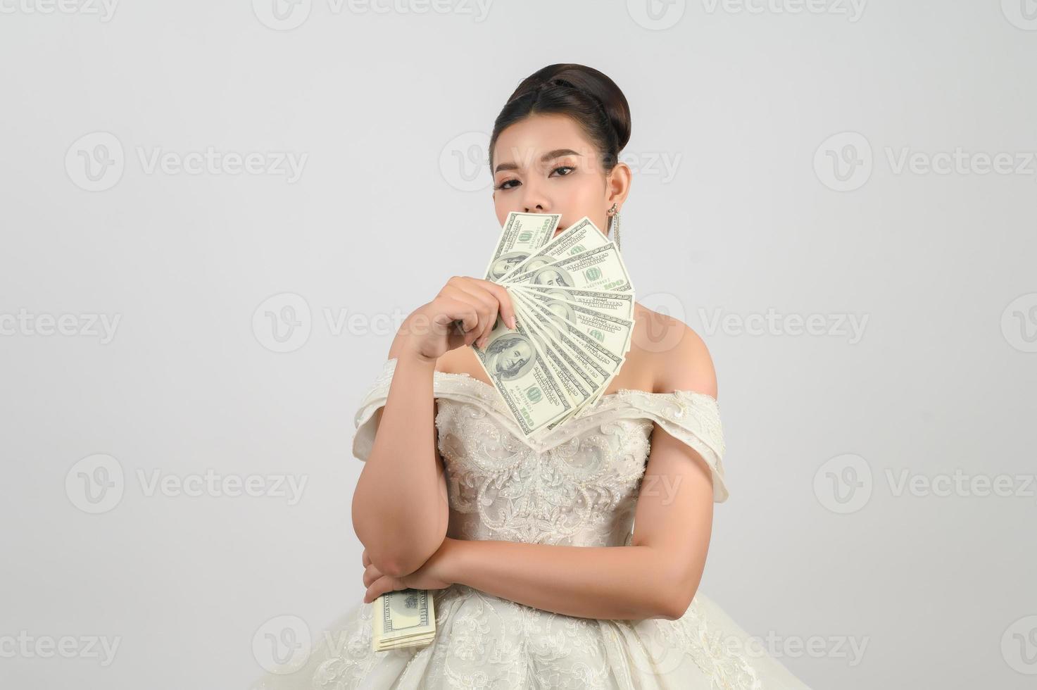 junge asiatische schöne braut, die in der hand dollarnoten hält foto