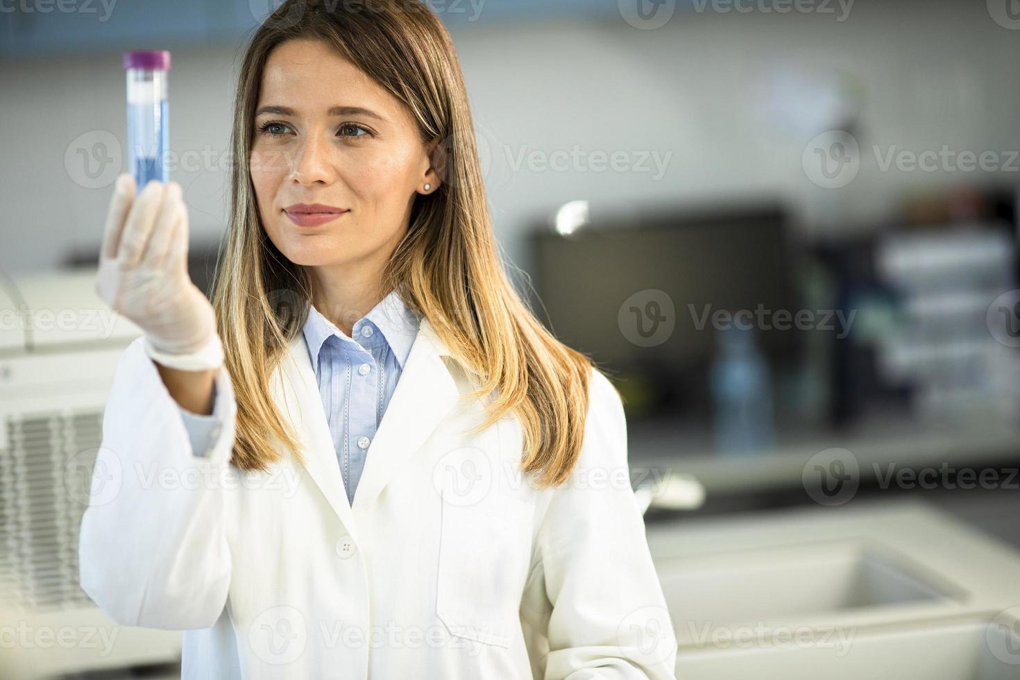 Ärztin mit schützender Gesichtsmaske im Labor, die den Kolben mit flüssiger Probe hält foto