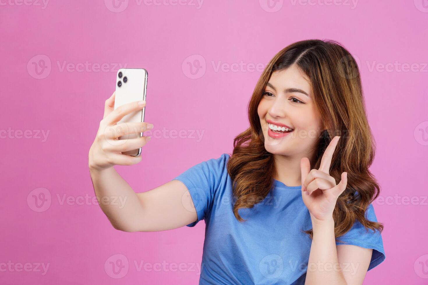 Porträt einer glücklich lächelnden jungen Frau, die ein lässiges T-Shirt-Selfie mit Smartphone trägt, das über rosafarbenem Hintergrund isoliert ist foto