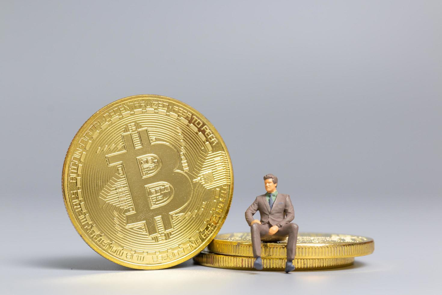 Miniaturgeschäftsmann, der auf Bitcoin-Münzen sitzt, zukünftiges Investitionskonzept foto