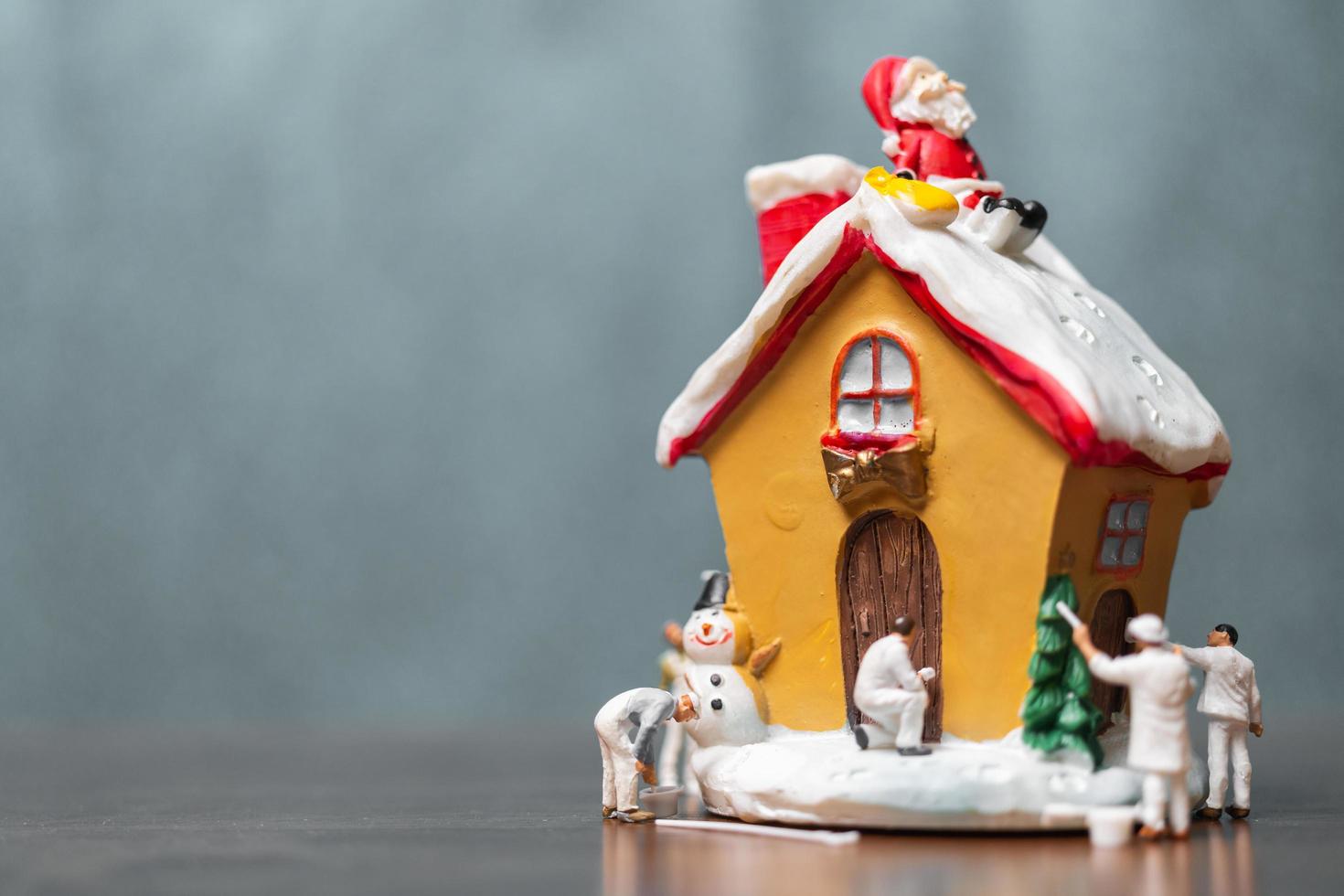Miniaturmenschen, die ein Haus und einen Weihnachtsmann malen, die auf dem Dach sitzen, frohe Weihnachten und frohe Feiertagskonzept foto