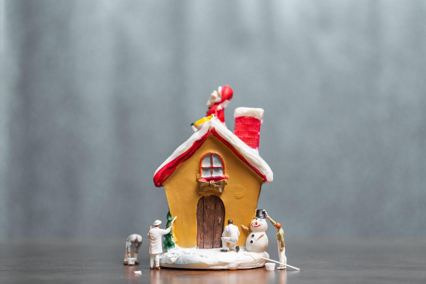 Miniaturmenschen, die ein Haus und einen Weihnachtsmann malen, die auf dem Dach sitzen, frohe Weihnachten und frohe Feiertagskonzept foto