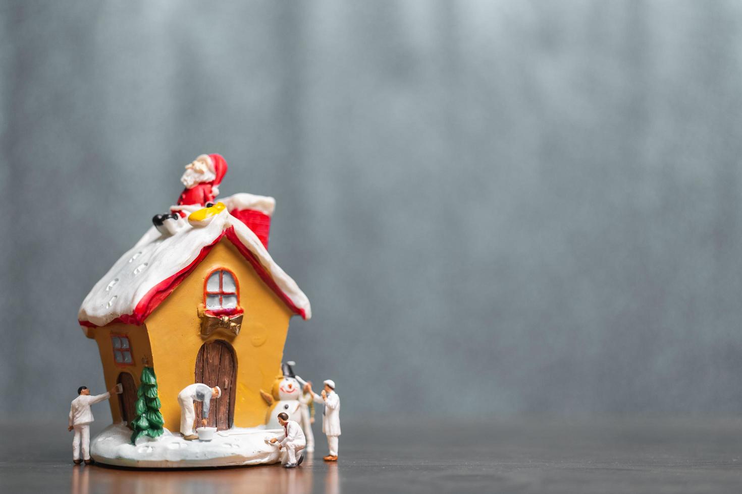 Miniaturmenschen, die ein Haus und einen Weihnachtsmann malen, die auf dem Dach sitzen, frohe Weihnachten und frohe Feiertagskonzept foto