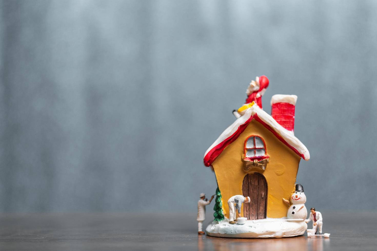 Miniaturmenschen, die ein Haus und einen Weihnachtsmann malen, die auf dem Dach sitzen, frohe Weihnachten und frohe Feiertagskonzept foto