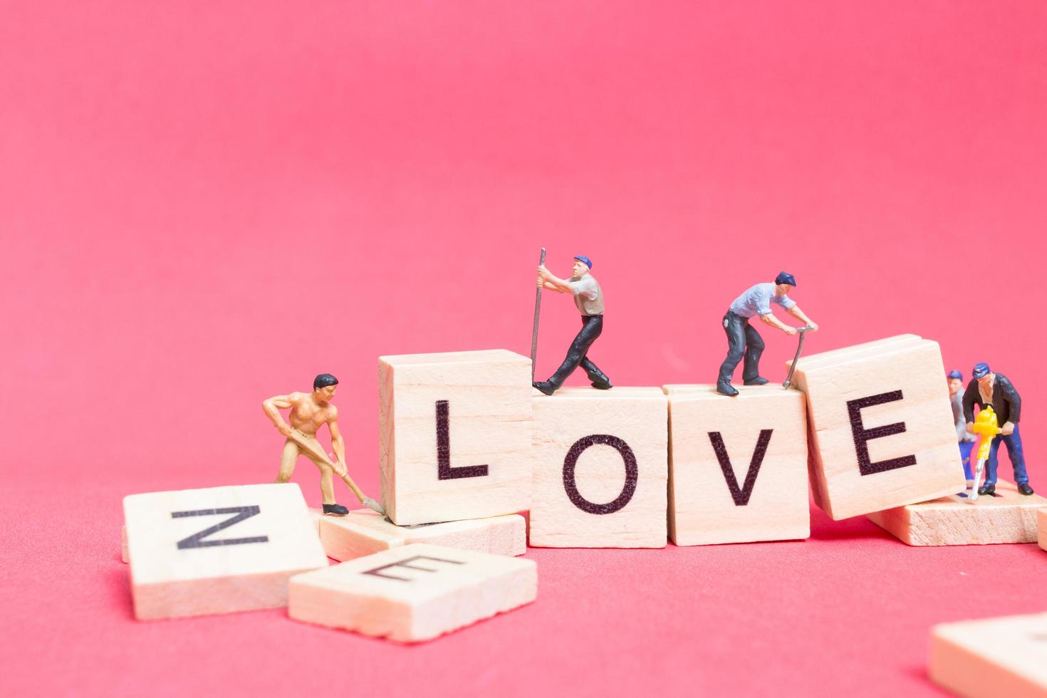 Miniaturarbeiter, die sich zusammenschließen, um das Wort Liebe auf Holzklötzen mit einem rosa Hintergrund, Valentinstagkonzept aufzubauen foto