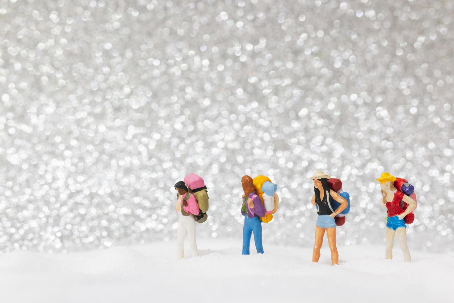 Miniatur-Rucksacktouristen, die auf einem Schneehintergrund, Winterkonzept gehen foto