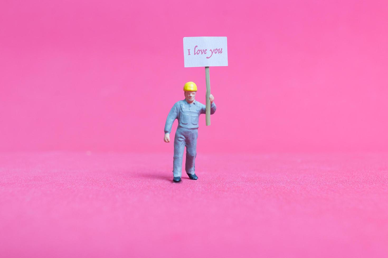 Miniaturperson, die eine Pappe mit ich liebe dich auf einem rosa Hintergrund, Valentinstagskonzept hält foto