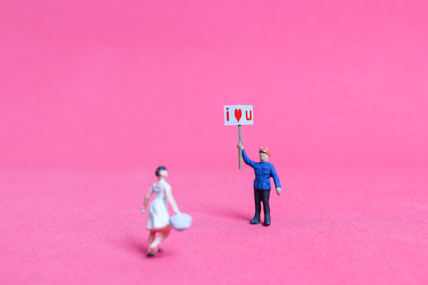 Miniaturperson, die eine Pappe mit ich liebe dich auf einem rosa Hintergrund, Valentinstagskonzept hält foto