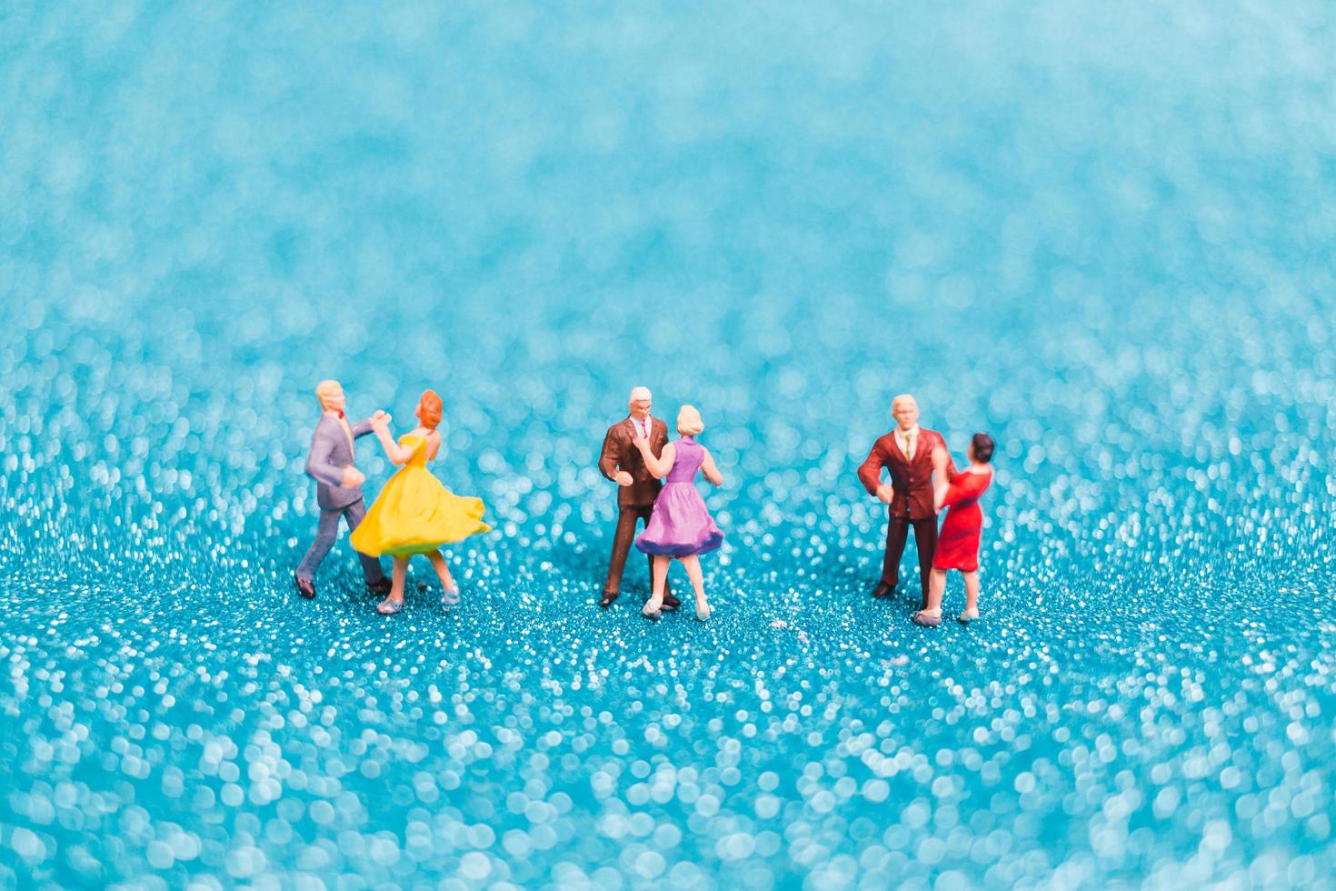 Miniaturpaare tanzen auf blauem Glitzerhintergrund, Valentinstagkonzept foto