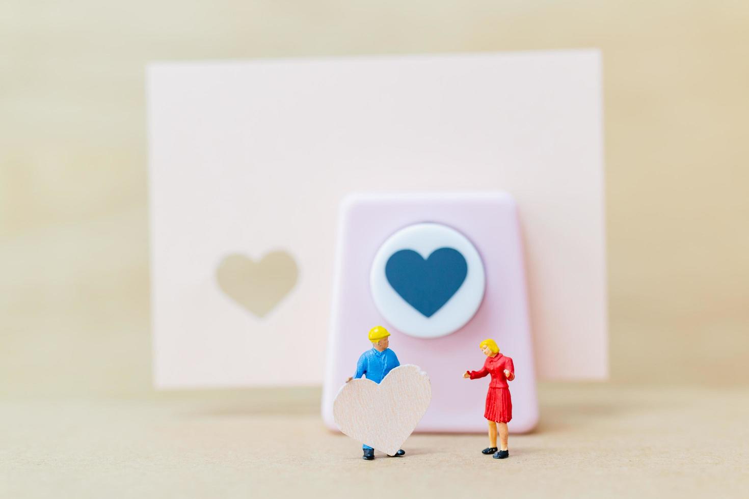 Miniaturpaar mit einem Papierherz auf hölzernem Hintergrund, Valentinstagkonzept foto