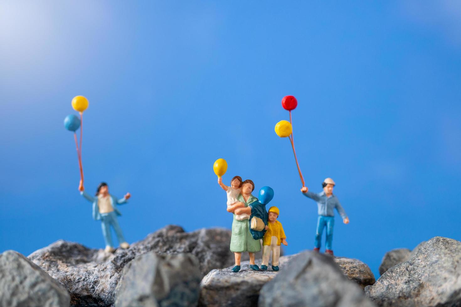 Miniaturfamilie, die Luftballons auf einem Felsen mit einem blauen Himmelhintergrund hält foto