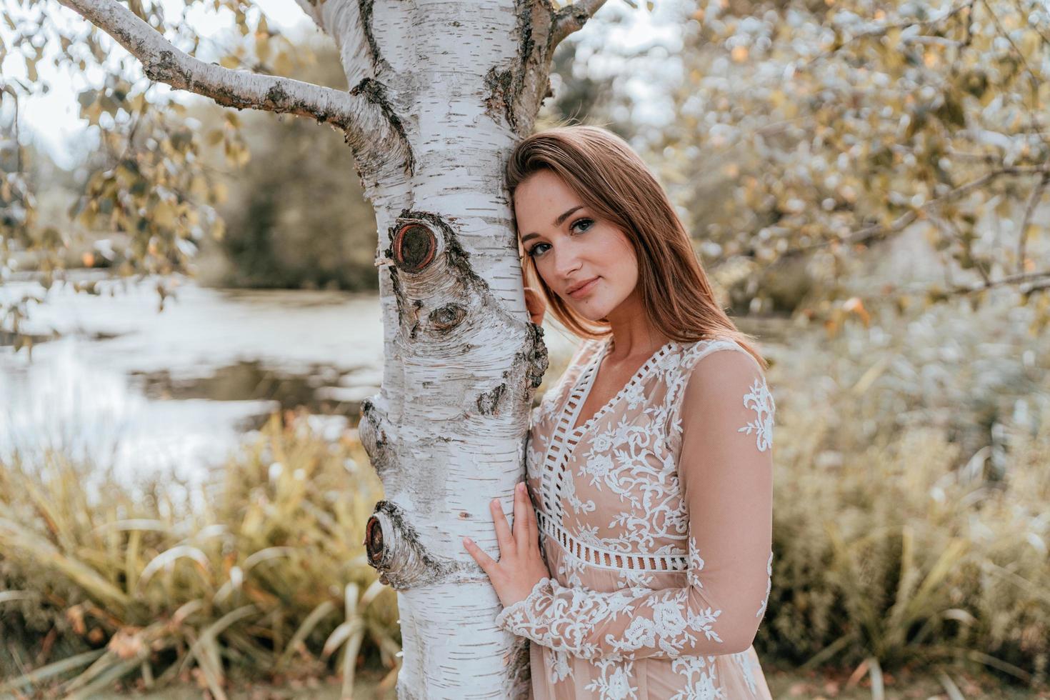 Frau posiert gegen einen Baum in einem Kleid foto