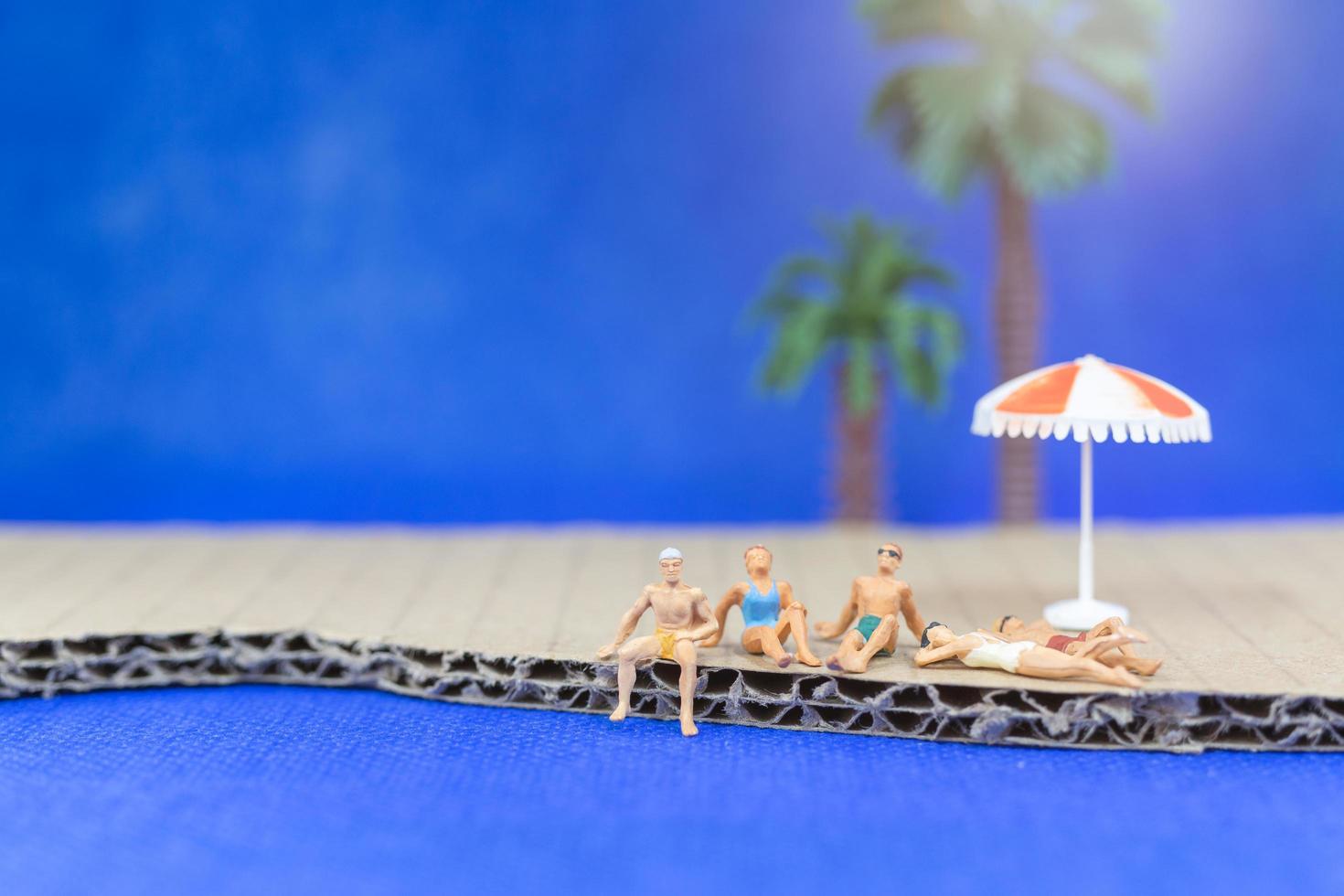 Miniaturmenschen, die Badeanzüge tragen, die auf einem Strand mit einem blauen Hintergrund entspannen foto