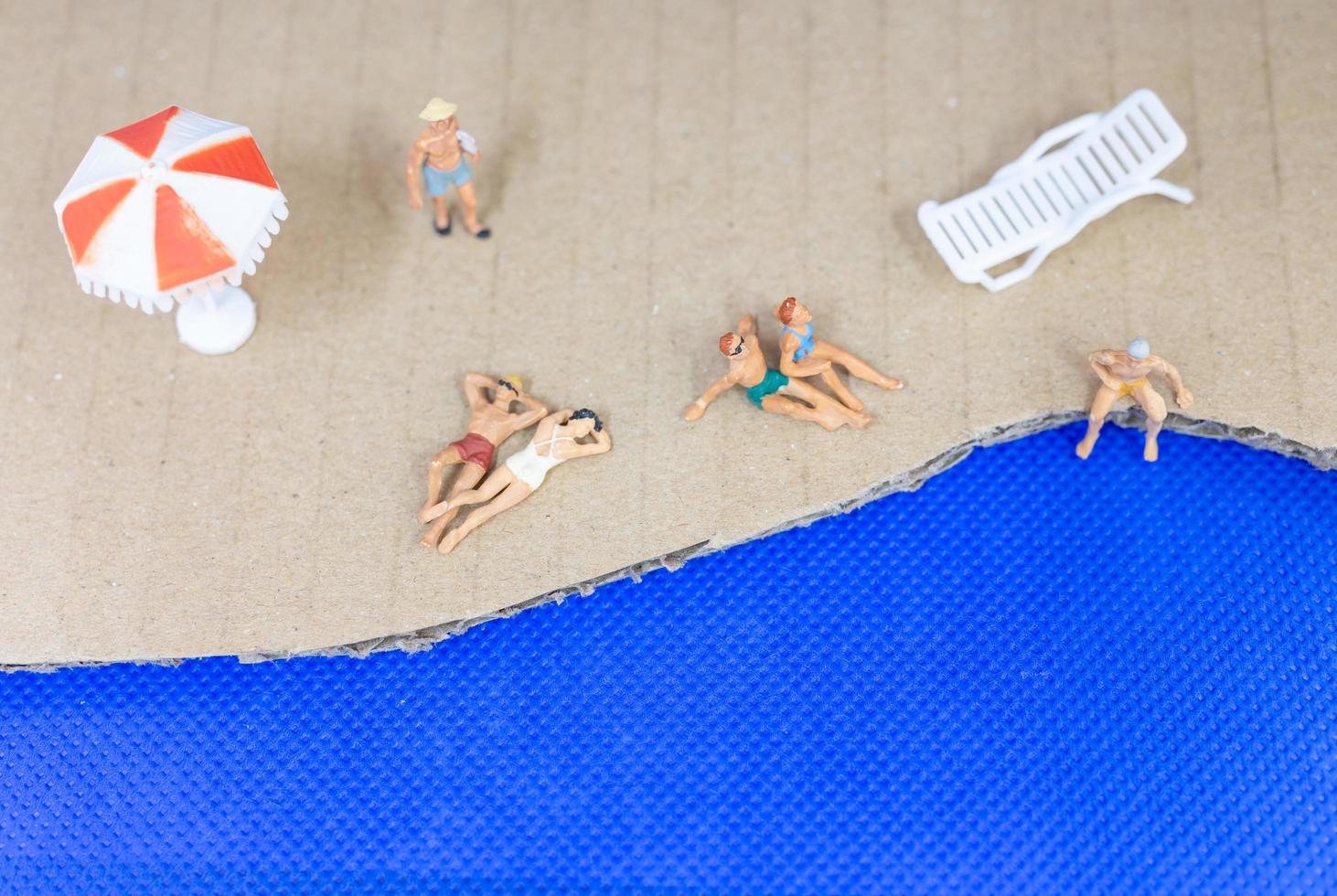 Miniaturmenschen, die Badeanzüge tragen, die auf einem Strand mit einem blauen Hintergrund entspannen foto